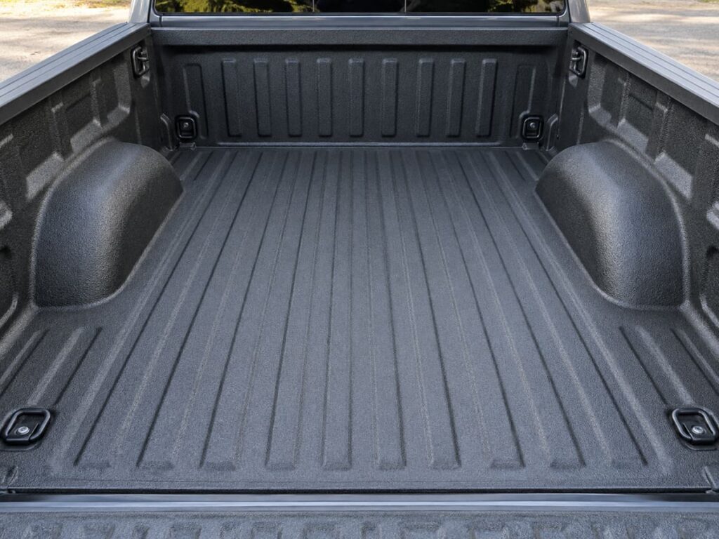 Vue en plongée d’une benne de pick-up vide recouverte d’un liner texturé, montrant le plancher, les passages de roue et les points d’ancrage.