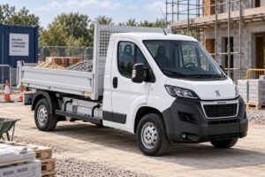 Utilitaire Peugeot Boxer avec benne basculante stationné sur un chantier professionnel, vu de trois quarts avant, avec un chargement sobre de matériaux.